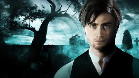 A man in a waistcoat stares straight ahead as a dark figure looms behind him in a cemetery 