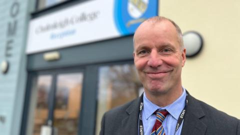 Michael Johnson, head teacher at Chulmleigh College, wearing a blue shirt, a burgundy striped tie, grey suit and a staff lanyard in front of the school