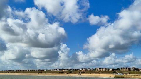 view of beach from sea with houses in distance under a cloudy, blue sky