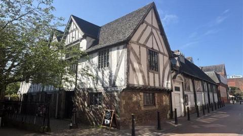 A timber-framed building on a pedestrianised street bathed in spring sunshine