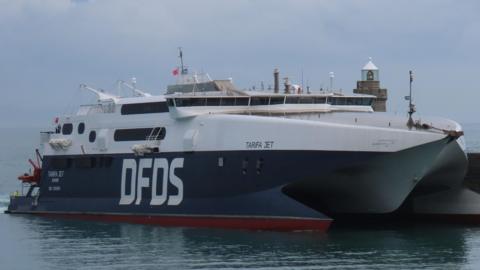 A picture of a large navy blue DFDS ferry. It is large with white font of the side saying DFDS.