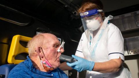 The Mid and South Essex respiratory testing bus run by Provide for the long covid service. It shows a nurse testing a patient for their lung capacity. The patient is wearing a blue top and the nurse is wearing white scrubs