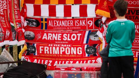 A wide shot of a child looking on at a selection of Liverpool scarves.