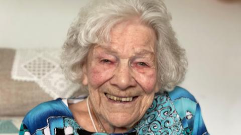 A older woman wearing a blue dress smiles at camera