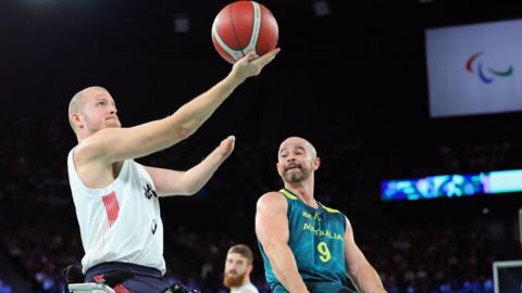 Kyle Marsh wearing a white tank top. He is lifting a ball as an opposing player looks on.