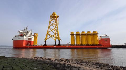 The heavy lift vessel Hua Yang Long sitting in port at Leith. It is mainly red and white but has a large yellow tower in the middle as well as large yellow cylinders.