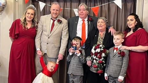 Three women, two men and three children taking a photo during a wedding renewal ceremony