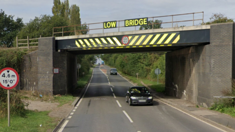 A railway bridge over a road.  It has a sign saying low bridge on it