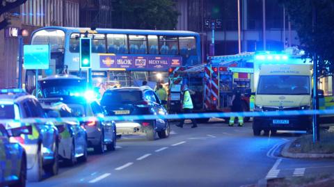 A night-time shot showing a bus, ambulance, fire engine and several police cars and police tapes on a town centre street 