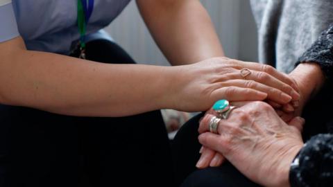A close up of nurse consoling and holding hands with senior patient.