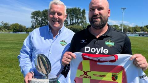 Gary Haycock-West (left) and Jordan Reynolds pose with the trophy being played for and a Channel Island shirt