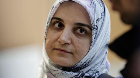 Mahdieh Esfandiari wears a white patterned head scarf and looks up towards a man in the right of the frame.