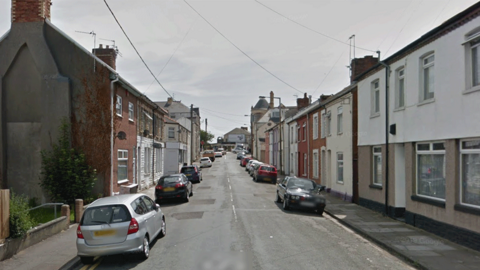 A row of painted terraced houses with cars lining either side of the road
