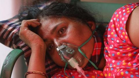 A woman wearing a pink dress and an oxygen mask suffering from breathing difficulty breathes with the help of an oxygen mask