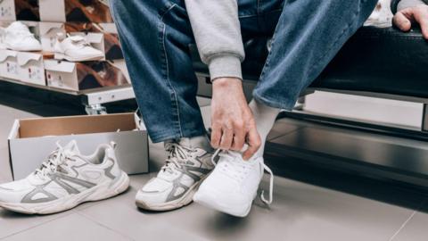 Man trying on white trainers in shoe shop