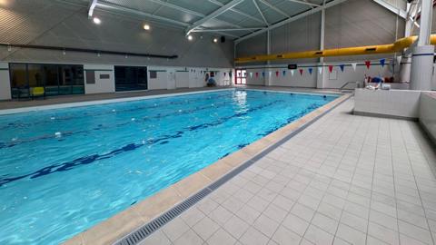 A wide photo of a corner of a swimming pool, taken from the side with tiled flooring in the background.