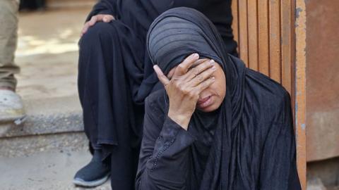 A woman sits on a stairway with her hand on her face, appearing distressed