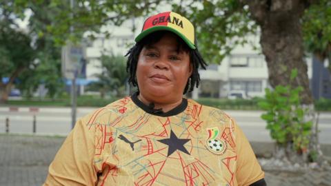 A woman with short braids wearing a Ghana jersey and hat.