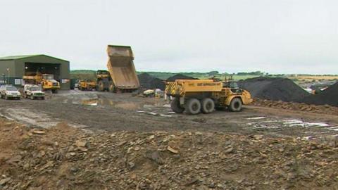 Dump trucks moving coal at Bradley Surface Mine. Piles of coal stand in the background.