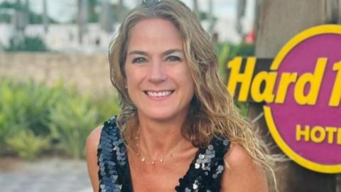 A woman in a black sequinned top on holiday against a Hard Rock sign