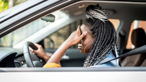 Woman in a car in the driver's seat holding her head in her hand, stuck in traffic - stock image