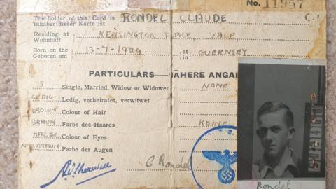 A German identity card with Claude Rondel's name, address and date and place of birth. It includes his single status, descriptions of his brown hair colour and hazel eyes. It has a small black and white passport style photo attached.