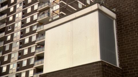 A boarded up window in a large brick tower of a housing block