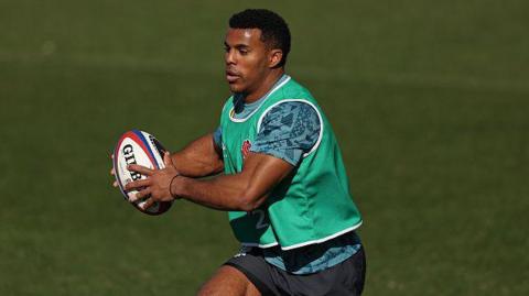 Immanuel Feyi-Waboso running with the ball during an England training camp. He has short black hair and is wearing a green bib with a blue training top and shorts.