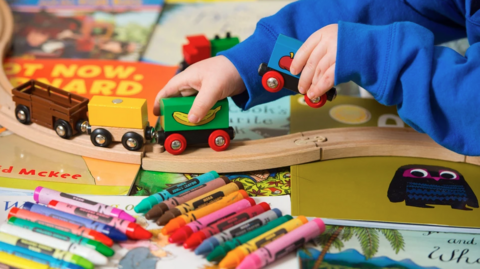 a child's hands push a toy train along a track in a nursery classroom