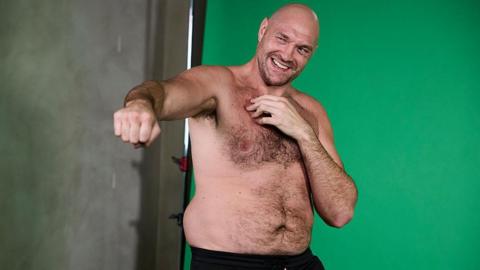 Tyson Fury poses with his fist out with his top off
