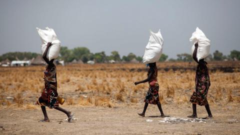 Three women carry a sack of food distributed on March 4, 2017, in Ganyiel, Panyijiar county, in South Sudan. South Sudan was declared the site of the world"s first famine in six years, affecting about 100,000 people.