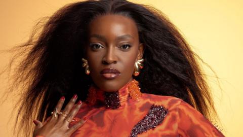 Woman wearing high neck orange top and pouting at the camera