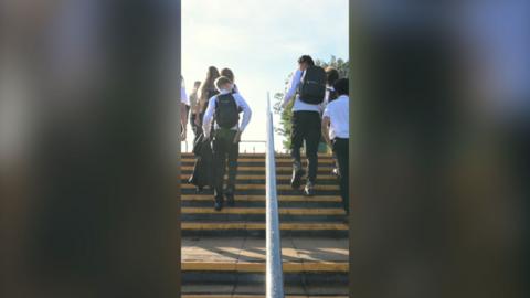 Boys in white shirts and black trousers walking up steps either side of a handrail.