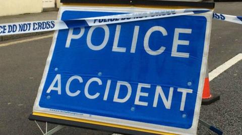 A picture of a police accident sign in the middle of a road. It is a blue sign with white writing on it.