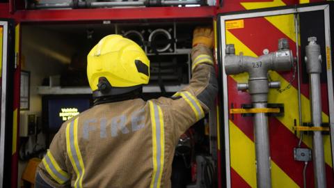 Stock photo of a firefighter reaching for an item inside a fire engine