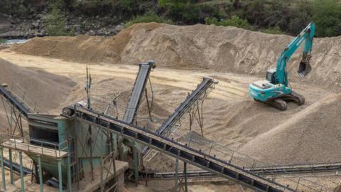 A stock image of a sand quarry, with a blue digger on site 