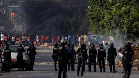 Riot police stand as a large plume of smoke rises near supporters