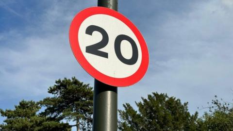 A circular sign on a post with a red outline and a black 20 on a white background.