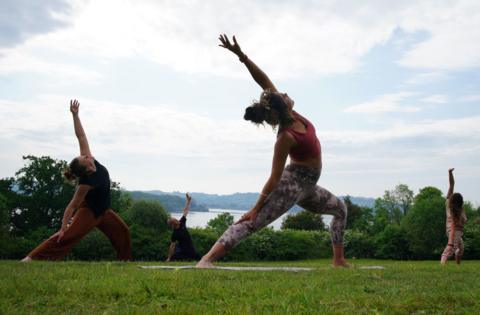 Three woman stretch in yoga poses on a green space next to Chew Valley Lake