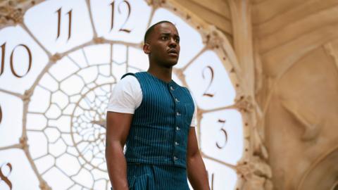 The Doctor standing in front of a huge clock face window.