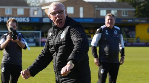 Steve Evans clenches his fists and shouts with his mouth open while walking on the pitch at the end of Bristol Rovers' win against Harrogate