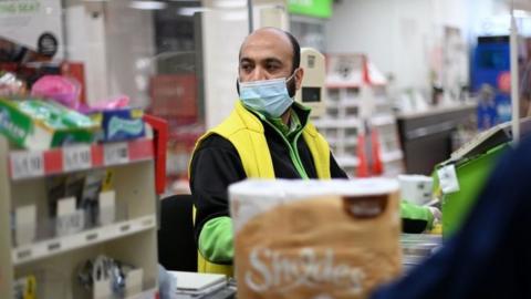 A shop worker wearing a protective face covering to combat the spread of the coronavirus, serves customers at an Asda supermarket in London