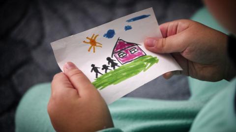 Child holding a drawn picture of a house and stick family