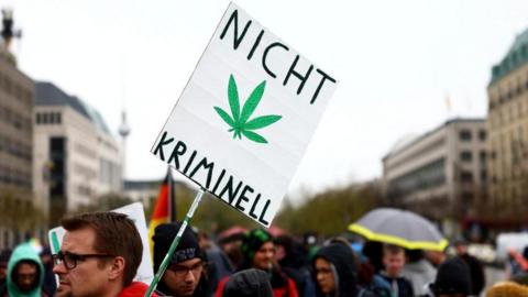 A man carries a sign with a drawing of a cannabis plant and words that say "Not criminal" as he participates in a protest calling for the legalisation of marijuana, in front of the Brandenburg Gate, in Berlin, Germany, 20 April 2022