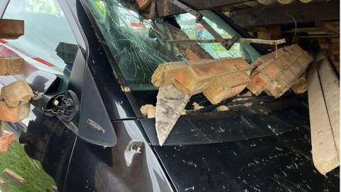 A damaged car that has smashed through a brick wall