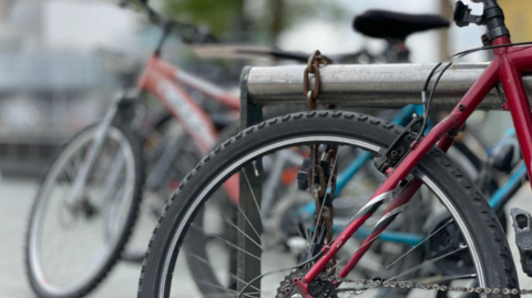 A mainly red bike with a black wheel is parked. Other bikes are blurred in the background.