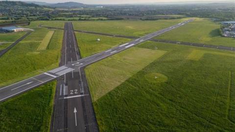 Two Gloucestershire Airport runways seen from the air on a sunny day, with countryside around