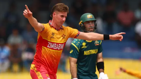 Brad Evans of Zimbabwe celebrates the wicket of Travis Head of Australia as Glenn Maxwell watches on from the non-striker's end