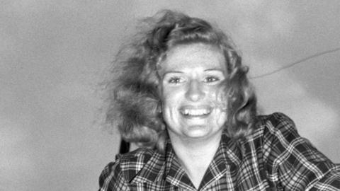 A black and white photo of Richarda Morrow-Tait with her hair blowing in the breeze, wearing a plaid shirt and smiling broadly