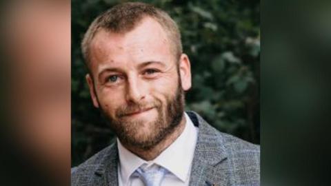 Max Richardson. A man with a beard wearing a suit smiling at the camera